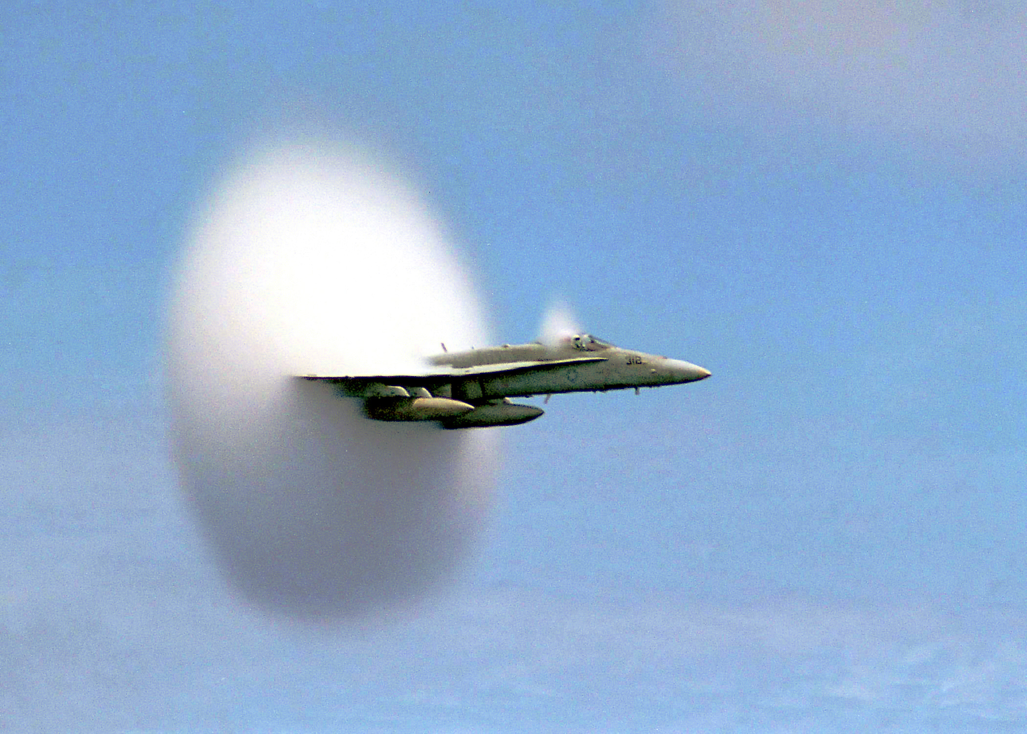A jet in flight enveloped by a cone-shaped white cloud of condensed water vapor.